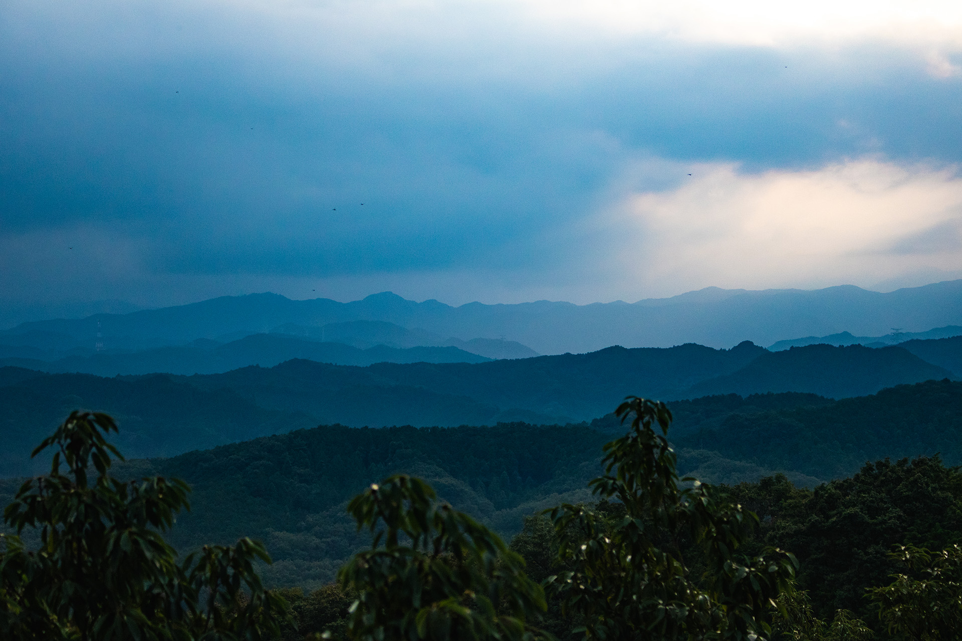 Dark landscape of green mountains fading into the fog in the distance.